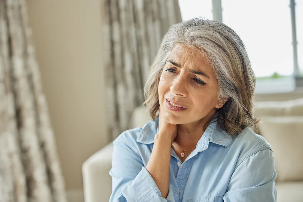 Mature Woman At Home Suffering From Muscle Pain Or Ache In Neck