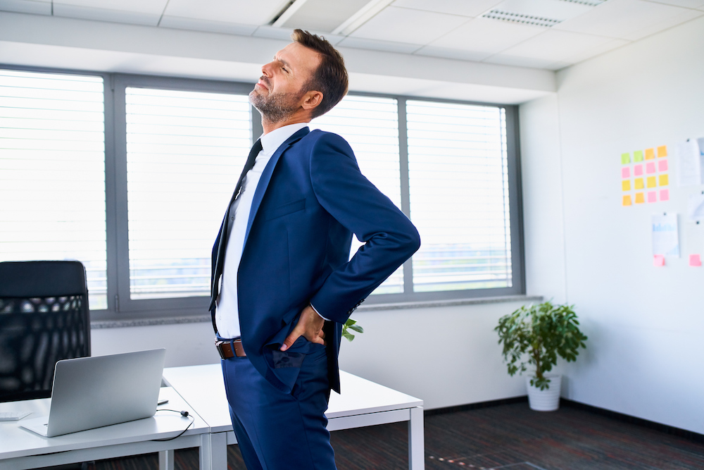 Lower back pain. Businessman stretches in office.